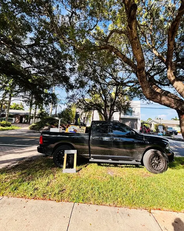 La camioneta negra de Eddy bajo un &aacute;rbol, cargada con una pizarra y muebles